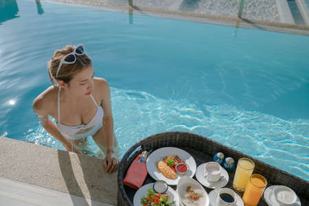 Happy woman relax with floating breakfast in swimming pool villa hotel resort.