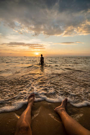 Woman silhouette on the beach at sunset with man legs.の写真素材