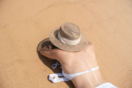 Back side woman in bikini lying down on sand beach relaxing sunbathing.