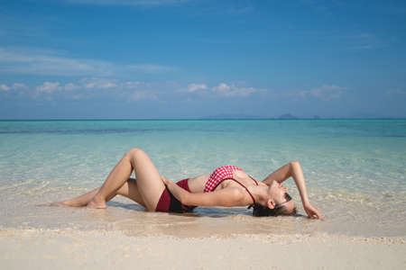 Woman in red bikini swimsuit laying on the sand beach in the clear water. summer vacation.の写真素材
