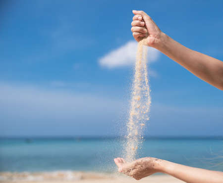 Woman pouring the sand from hand to hand on the beach, blue sky.の写真素材