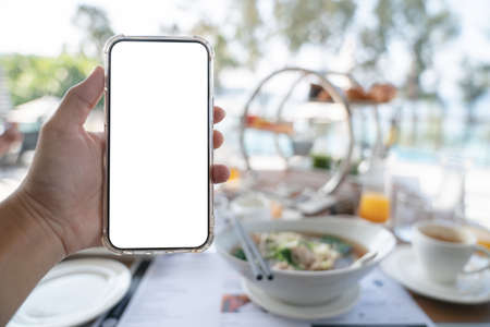 Woman hands holding blank screen mockup phone, order food online concept, breakfast background.の写真素材
