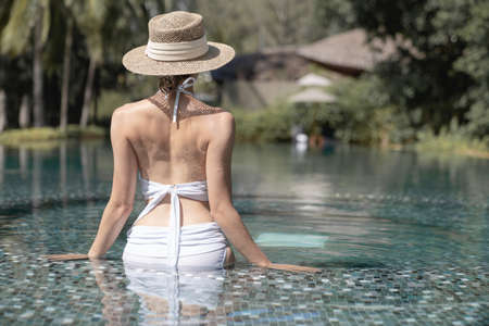 Back side of woman wearing bikini and straw hat relaxing in pool. spa treatments concept.の写真素材