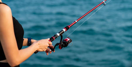 Woman hand holding fishing rod with sea background, fishing at sunset.の写真素材