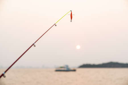 Artificial small fish on a fishing rod with sea background, fishing at sunset.の写真素材