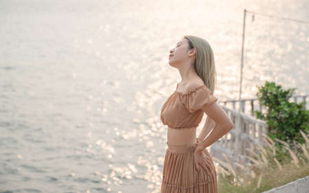 Asian woman wearing dress posing on the beach, golden sea sunset moment.の写真素材