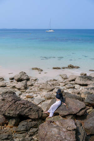 Woman in black bikini on tropical beach. Portrait woman in swimwear enjoying and sitting on rock beach.の写真素材