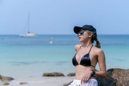 Woman in black bikini on tropical beach. Portrait woman in swimwear enjoying and sitting on rock beach.の写真素材