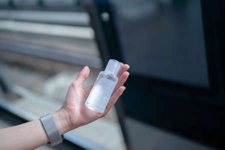 Woman wearing mask and using alcohol gel sanitizer to disinfect Covid-19 virus in metro train station.の写真素材