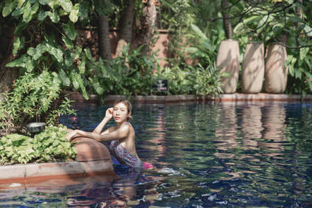 Woman in pink one piece swimsuit relax in tropical swimming pool, summer vacation.