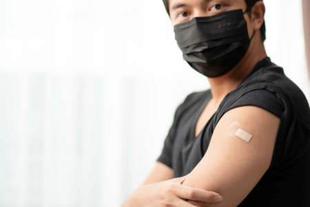 Man wearing mask arm with bandage showing his arm after receiving vaccine.