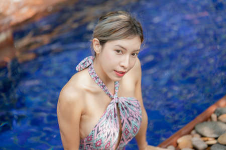 Woman in pink one piece swimsuit relax in tropical swimming pool, summer vacation.