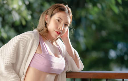 Woman wearing purple bikini with bathrobe standing on a wooden balcony with the garden and river view.の写真素材