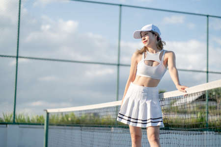 Woman tennis player in a white skirt resting on a tennis court.の写真素材