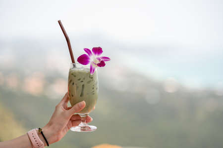 Hand holding green tea matcha latte cold beverage drink with orchid flower.の写真素材