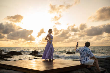 Couple in love man taking photo woman on the beach, enjoy sunset romantic moment.の写真素材