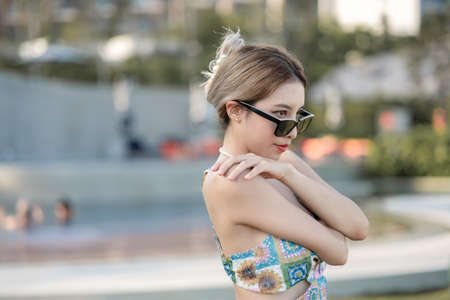 Woman wearing dress and sunglasses wrap arm around body, hug her self relaxing on tropical beach.