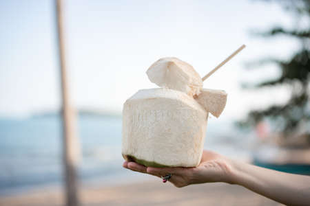 Fresh coconut cocktail in hand over ocean background.の写真素材