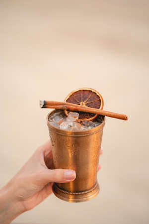 Hand with cocktail, Alcoholic drink with ice, orange and cinnamon on the beach.の写真素材