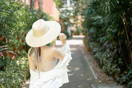Back view of woman wearing white shirt, long skirt and straw hat posing tropical garden.の写真素材