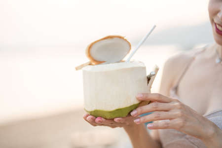 Woman drinking fresh coconut on the beach, romantic sunset moment. summer vacation.の写真素材
