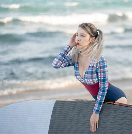 Woman wearing one-piece swimsuit hold sup board or paddle board to the sea.