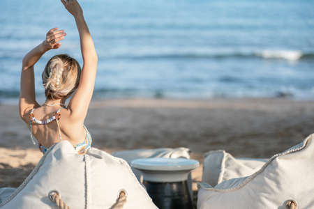 Woman raised hands up in the sky, relaxing on bean bag beach chair near the beach.