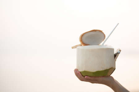 Hand holding fresh coconut on the beach, romantic sunset moment. summer vacation.