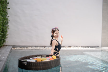 Woman relaxing and eating floating breakfast in the pool on luxury villa.
