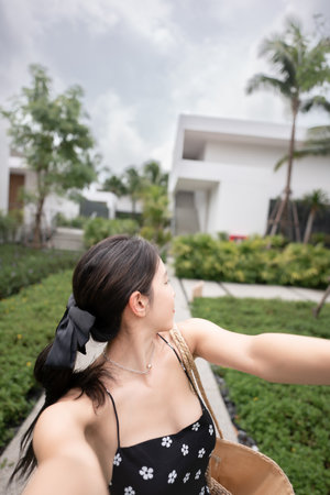 Woman in black dress with straw basket, walking in tropical resort hotel.の写真素材