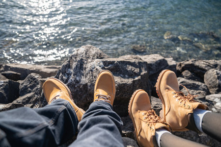 Legs in jeans and hiking boots on the rocks near mountain lake with water reflection.の写真素材