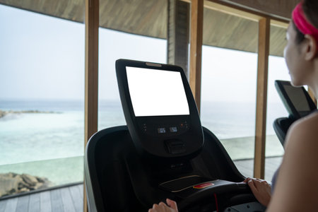 Woman is working out in gym. Doing cardio training on treadmill with white screen mockup , large...