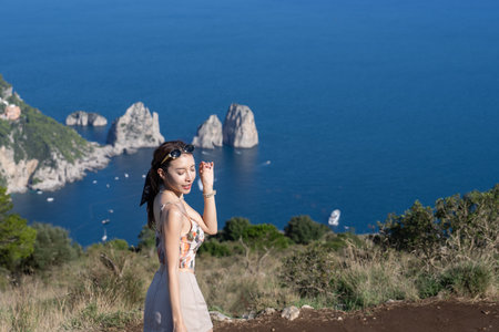 Woman enjoy view of beautiful coastal cliffs faraglioni di mezzo from Monte Solaro in Capri, Italy.の写真素材