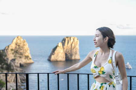 Woman enjoy view of beautiful coastal cliffs faraglioni di mezzo from Giardini di Augusto in Capri, Italy.の写真素材