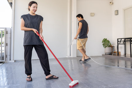 Couple cleaning garage floor with brush.