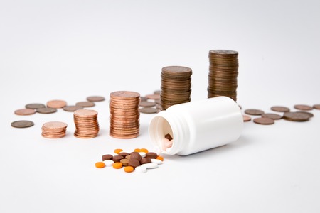 a stack of coins behind a white medication bottle and some medication spill on the tableの写真素材