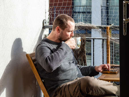 the man is drinking coffee on the balcony on a sunny day