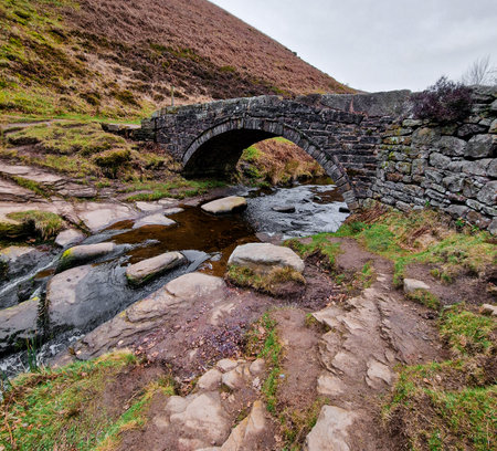 Three Shire Heads, where water cascades over mossy rocks and a packhorse bridge arches over the stream. Lush, rolling hills of the Peak District embrace this enchanting meeting pointの写真素材