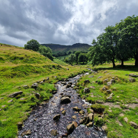 On a beautiful summer day, with the sun shining brightly and a few delicate clouds dotting the azure sky, a stroll by the Dovestone Reservoir offers a refreshing retreat. The calm waters of the reservoir mirror the sky, creating a mesmerizing blend of blue hues.の写真素材