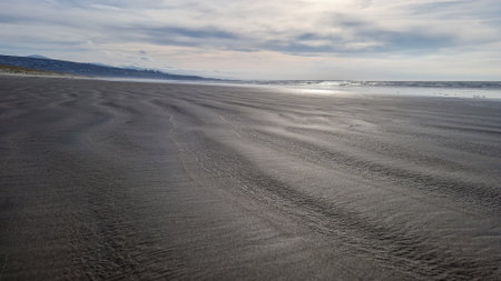 The warm hues of the setting sun cast a serene glow over the dunes of Harlech Beach in Wales, with the distant hills creating a tranquil coastal scene. The patterns in the sand and the wispy sea grass foreground lend a texture that speaks to the calmness of this Welsh shoreline.の写真素材
