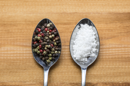Salt and pepper on metal spoonsの写真素材