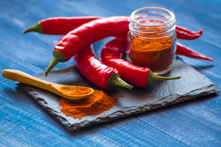 Red hot chili peppers and paprika powder on a blue wooden background