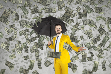 Young rich businessman standing in money rainの写真素材