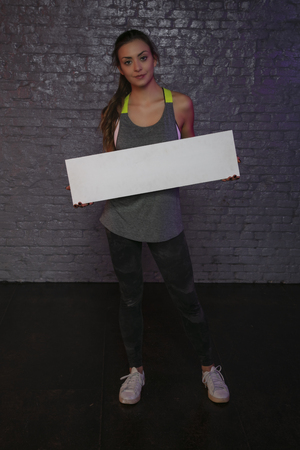 beautiful young girl holding an empty board, copy space for advertising, muscles and gym, conceptual photo, advertising spaceの写真素材