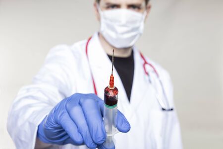 doctor holds a syringe in his hand filled with red liquid, concept of blood sampling or vaccineの写真素材
