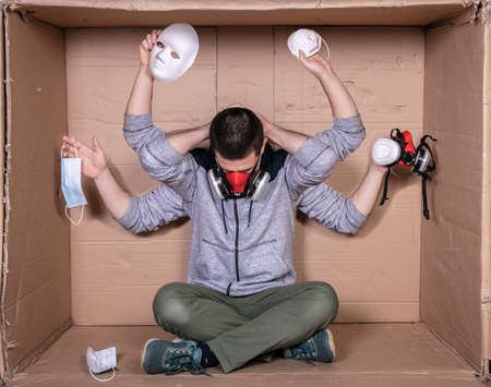 young worker sitting in a cardboard office puts a mask on his face and shows the types of masksの写真素材
