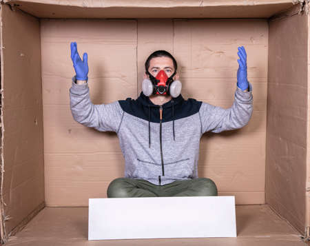 man in a protective mask sits at a cardboard box, showing his helplessnessの写真素材