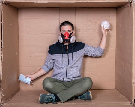 young worker sitting in a cardboard office with a mask on his faceの写真素材