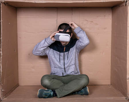 man with glasses for virtual reality, sitting in a cardboard room and entertainedの写真素材