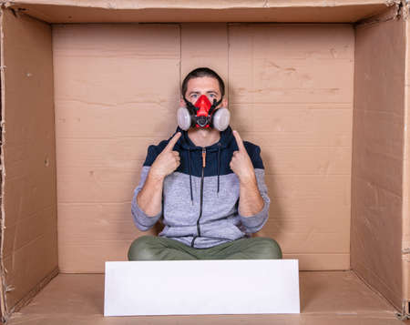 young worker sitting in a cardboard office with a mask on his faceの写真素材